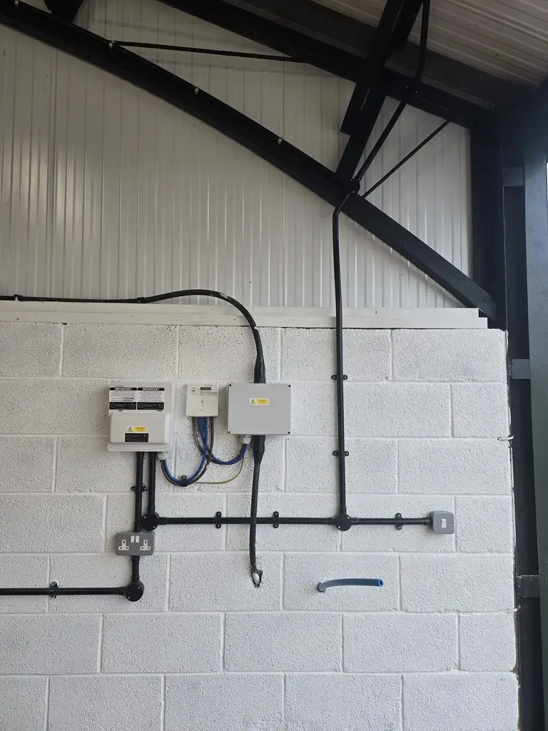 Electrical boxes and conduit mounted on a white brick wall.
