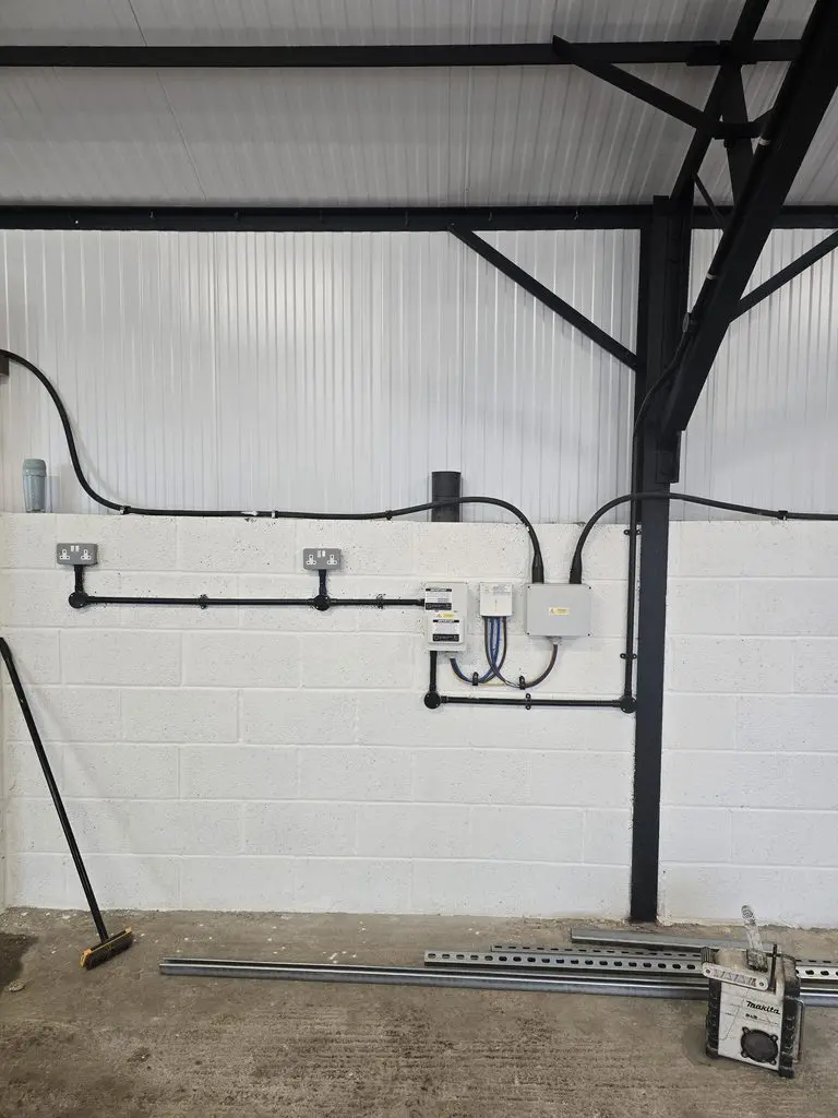 White block wall with two electrical outlets, junction boxes, and black conduit wiring, with a broom and Makita tool case on the concrete floor.