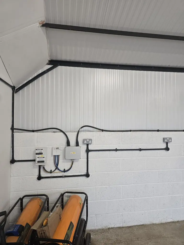 Electrical equipment and conduit installed on a white masonry wall, with two orange portable heaters on the floor below.