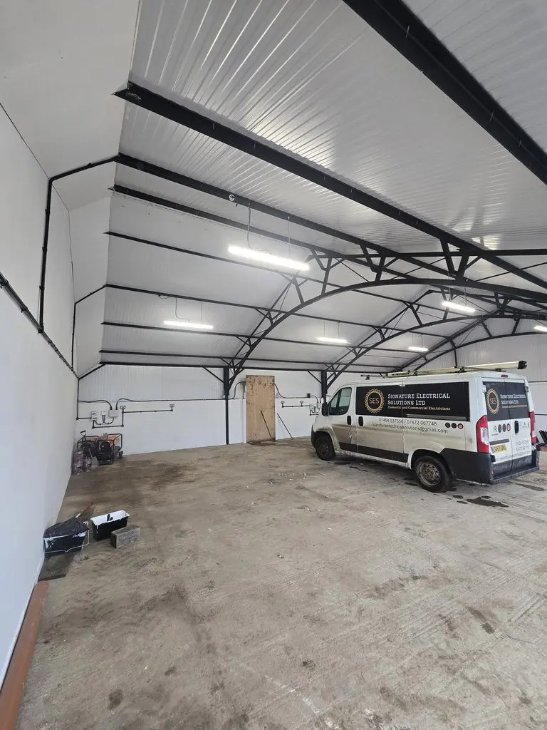 A white Signature Electrical Solutions van parked inside a large, empty metal-frame warehouse.