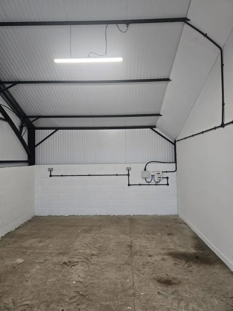 An empty storage room with white block walls, a corrugated metal ceiling, a single overhead light, and exposed electrical conduit.