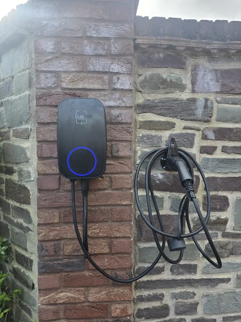 Electric vehicle charging station mounted on a brick wall with a cable coiled on a holder.