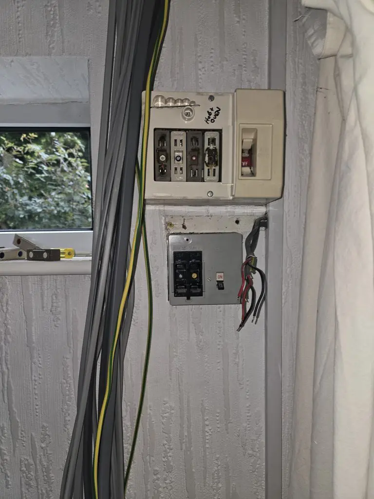 Electrical consumer units mounted on a wall with loose electrical wiring hanging nearby.