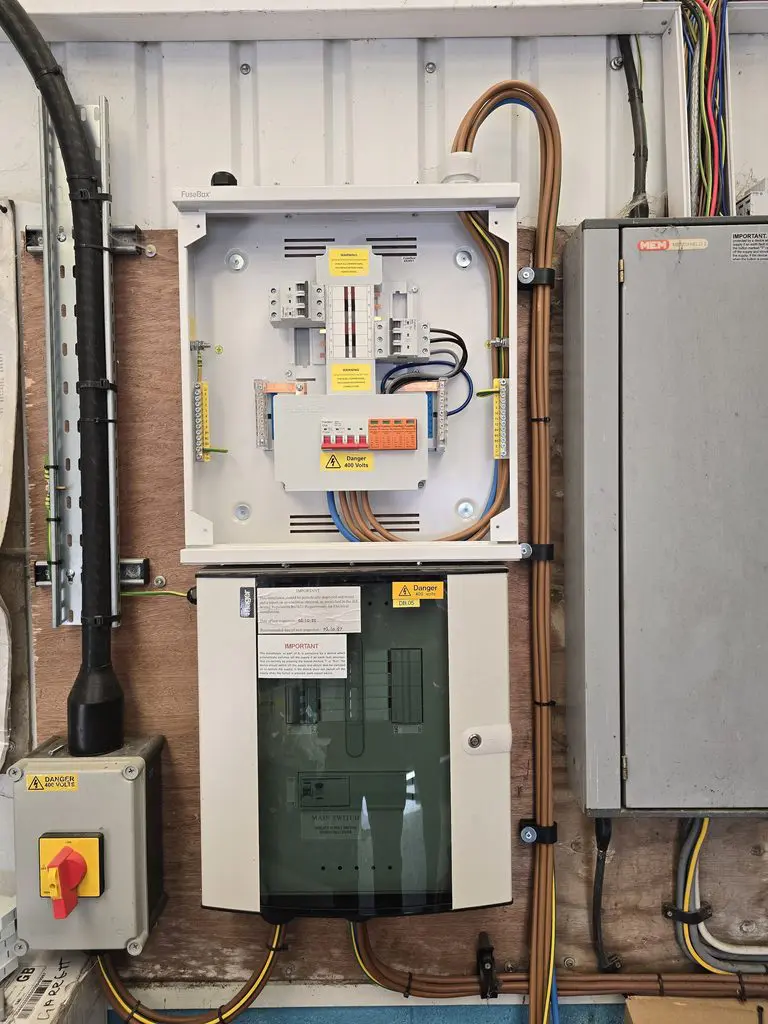 Two electrical distribution boards mounted on a wooden wall, with an isolator switch on the left and various wiring conduits.