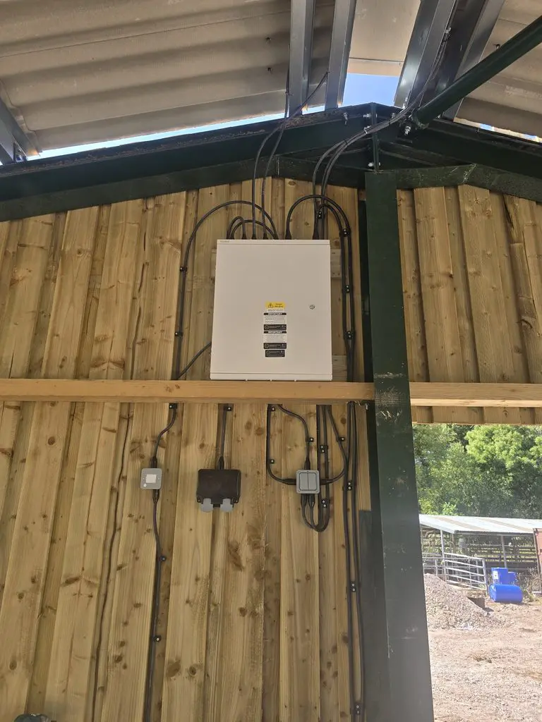 A white electrical distribution box mounted on a wooden wall, with cables running to smaller junction boxes below.