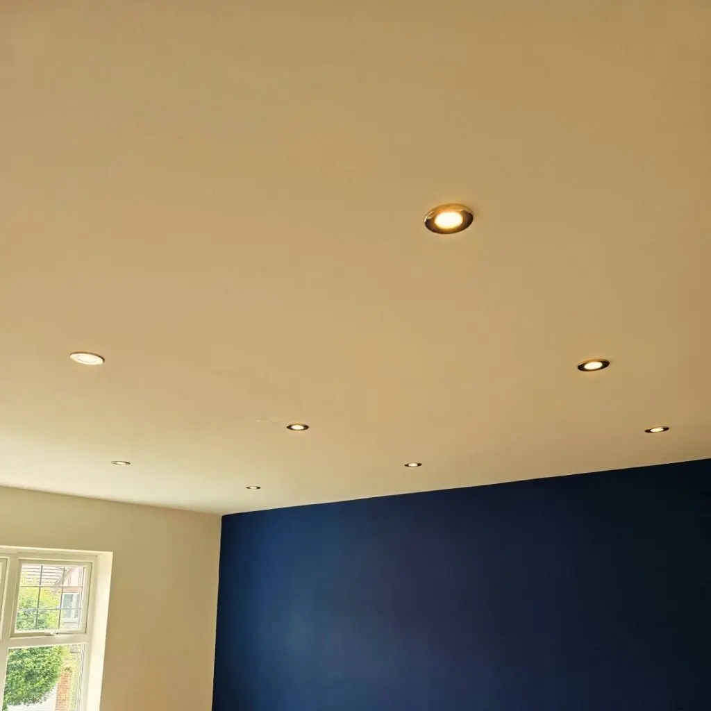 A room with a white ceiling featuring several recessed lights and a dark blue accent wall.