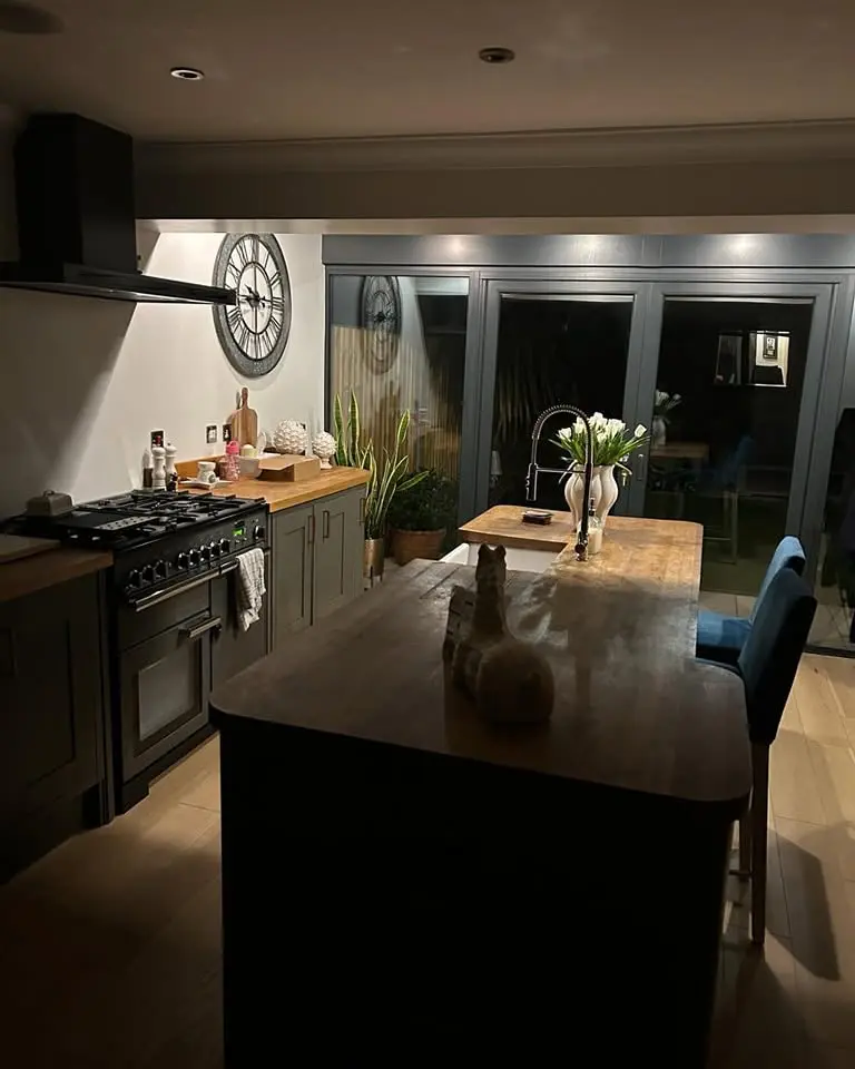 A kitchen featuring a wooden island with blue bar stools, a black stove, and a large round wall clock.