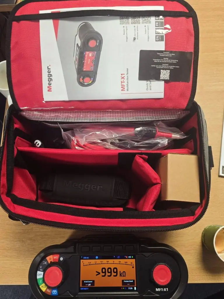 An open Megger MFT-X1 tester carrying case containing accessories, a user manual, and the tester device displayed in the foreground.