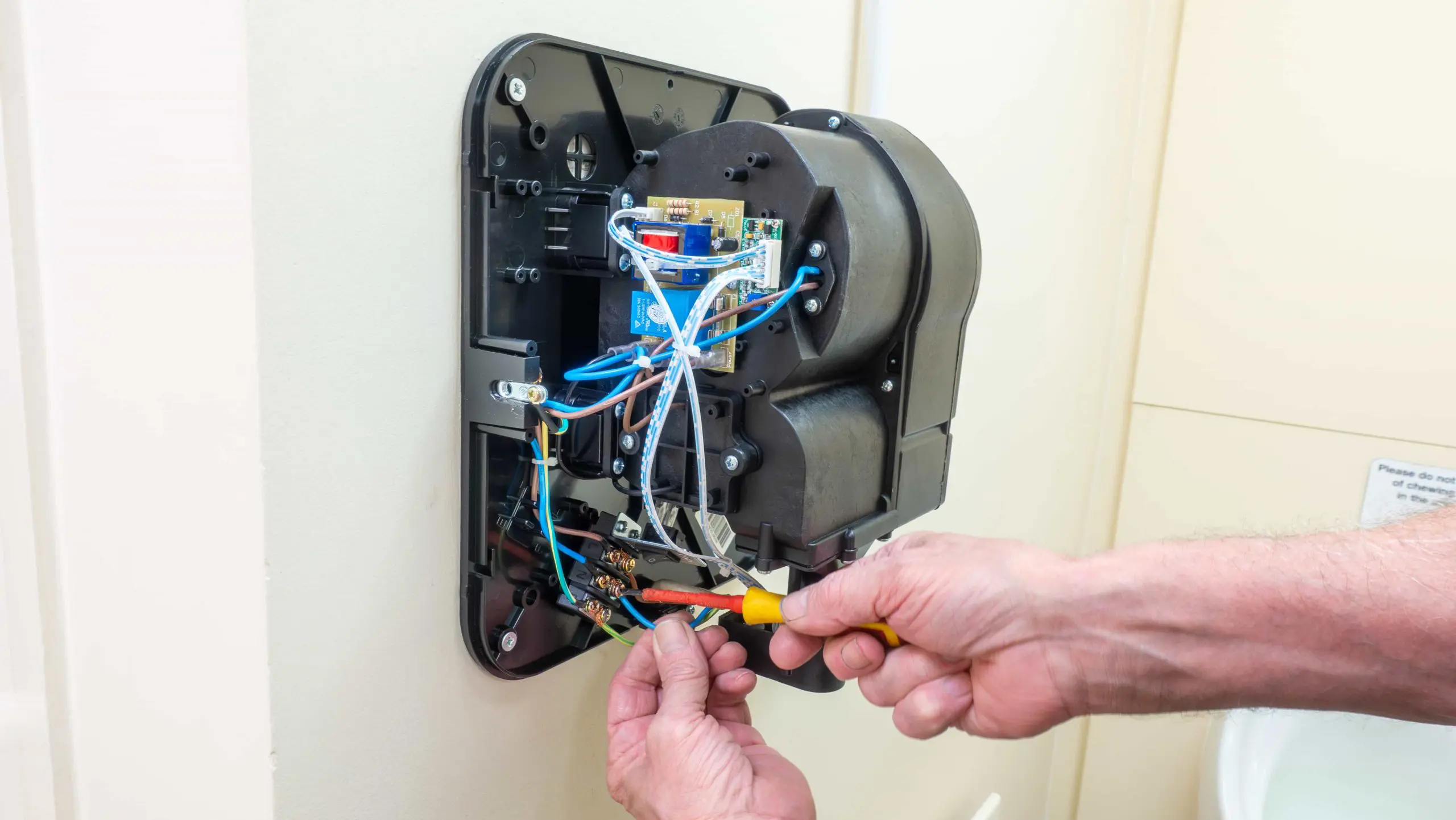 A person uses a screwdriver to wire a wall-mounted hand dryer.