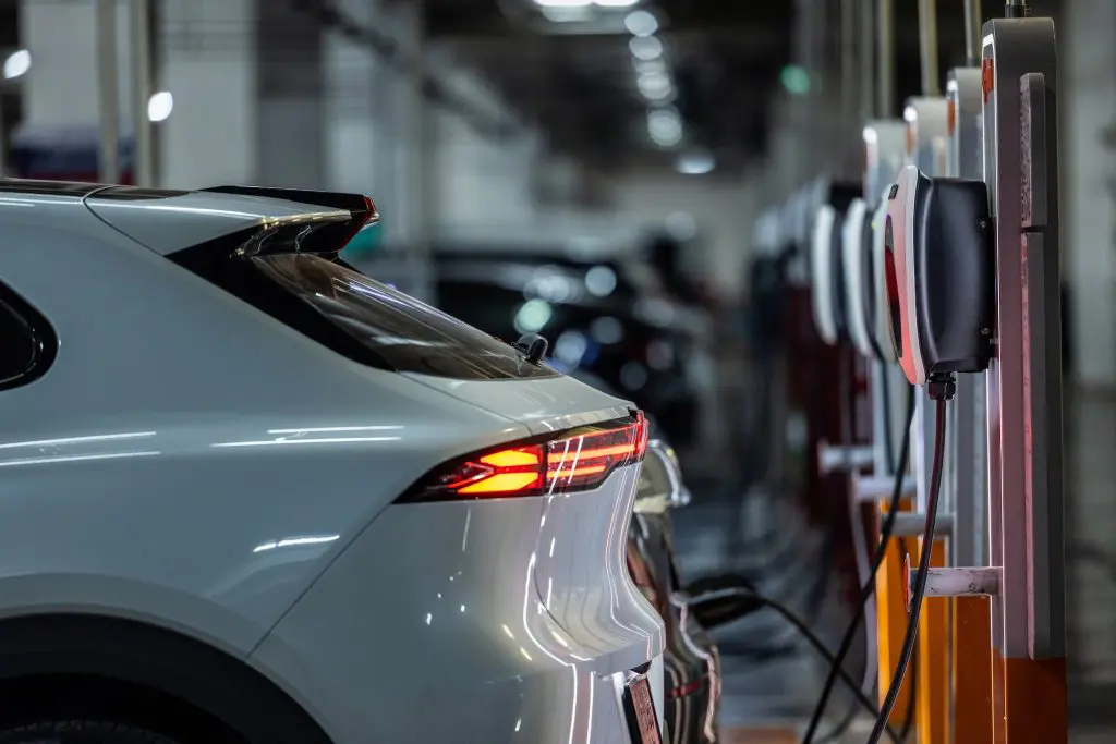 An electric vehicle charging at a station with a row of chargers in a parking garage.