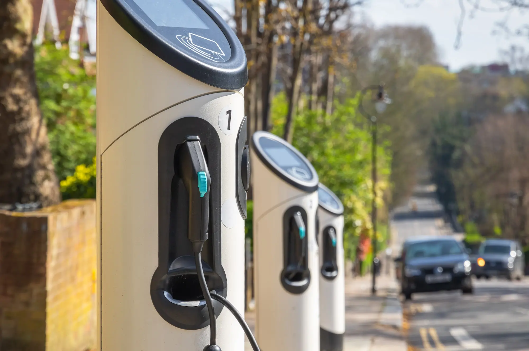 A row of electric vehicle charging stations installed on a sidewalk beside a street.