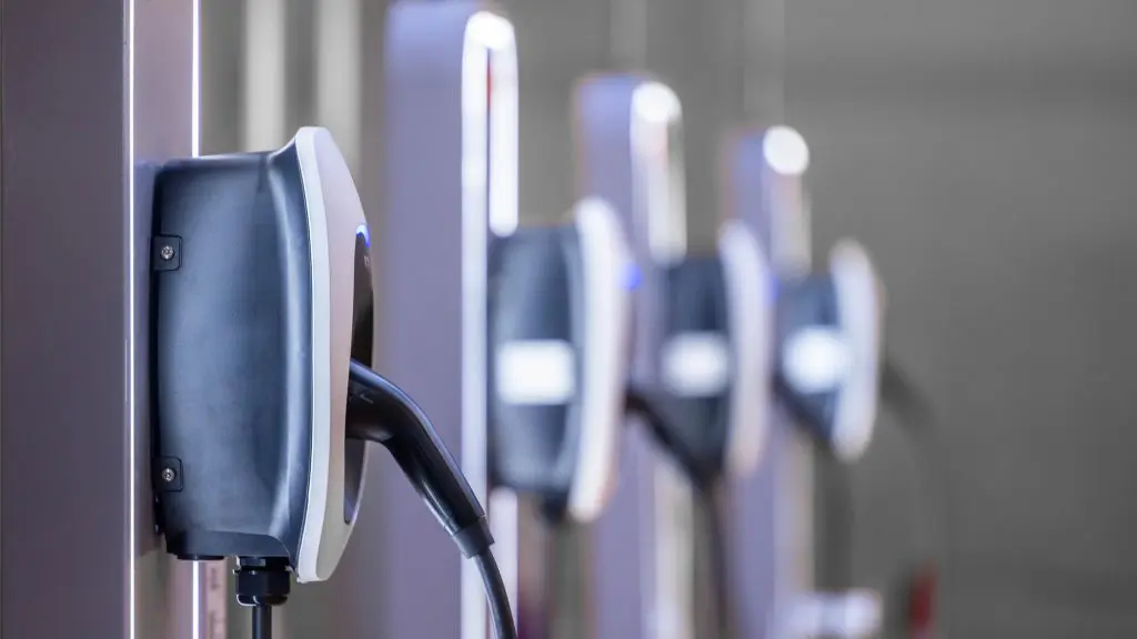 A row of electric vehicle charging stations with charging cables plugged into the first unit.